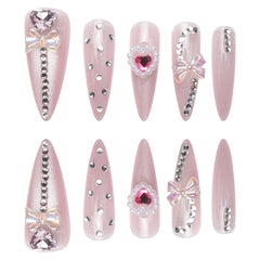 Pink cat eye press-on nails in long stiletto style, adorned with rhinestones and bows for a glamorous look.